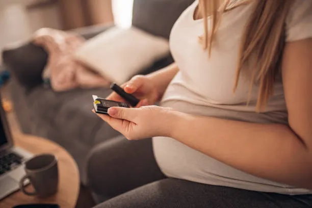 Gestational Diabetes - drpallavichauhan Pregnant woman sitting on a couch, holding a credit card and looking at her smartphone.